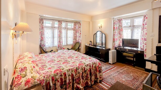 A bedroom with a bed, a desk, a chair, a TV, and a radiator.