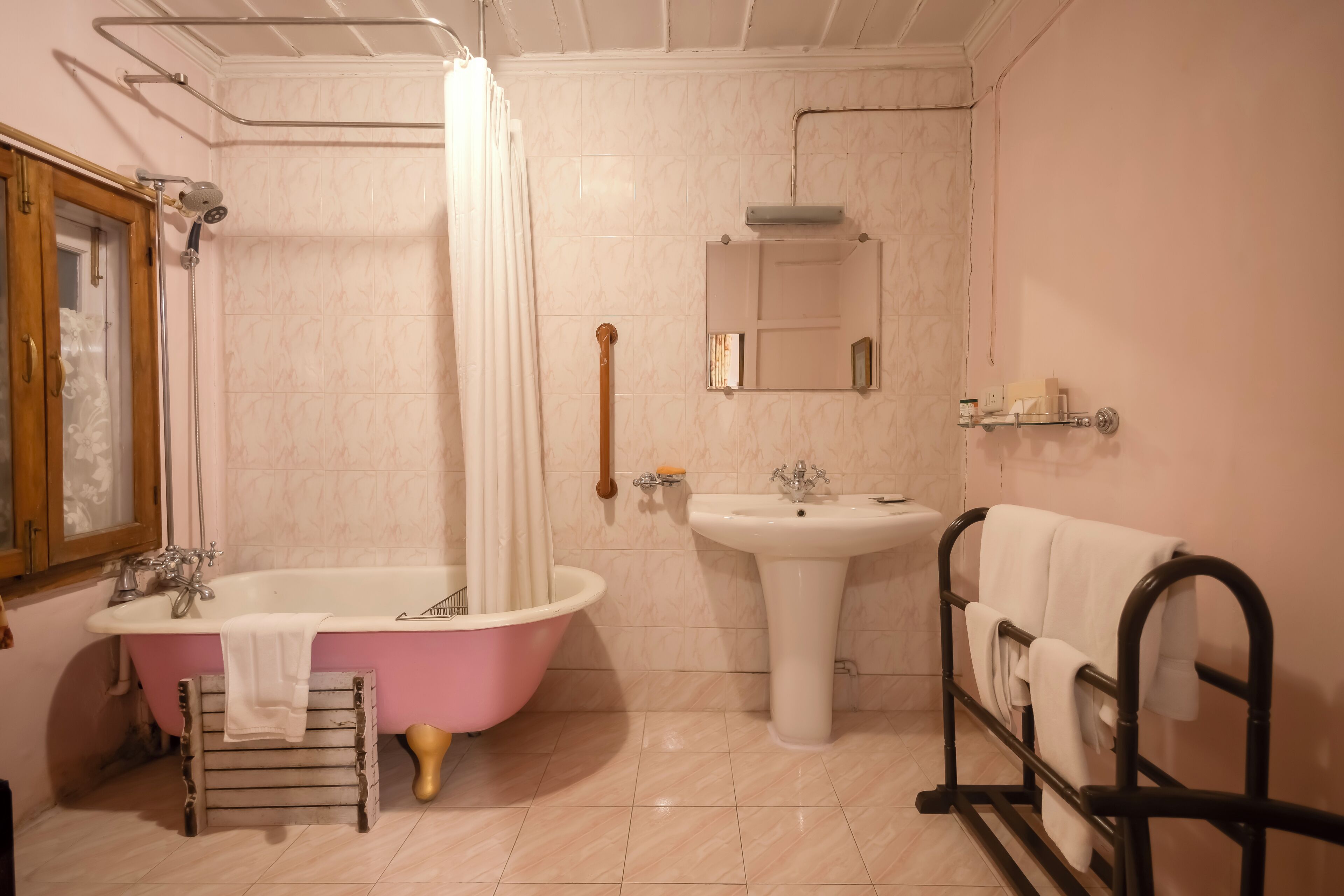 A bathroom with a pink bathtub, a white sink, a mirror, and a towel rack.