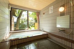 A bathroom with a bathtub, a shower, and a window with a view of greenery. - Grand Hotel Seifuso (Omuta)