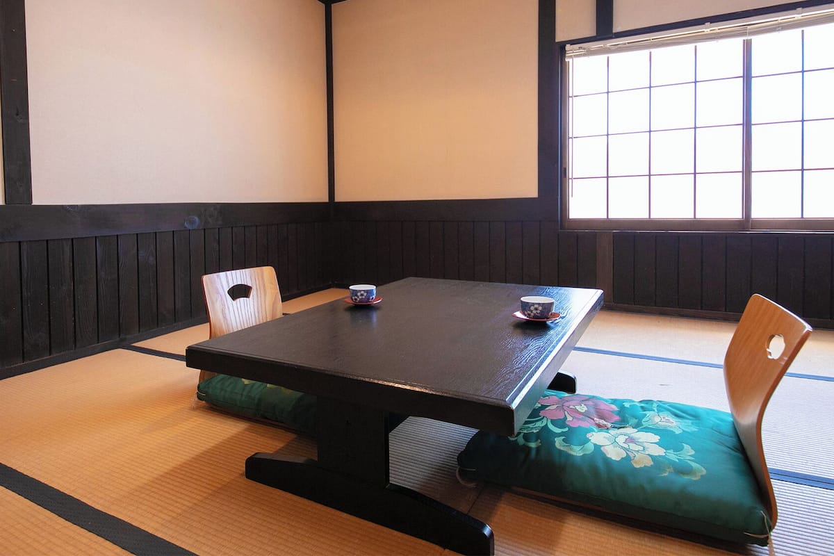 A tatami mat room with a low table, two cushions, and a window with grid panes.