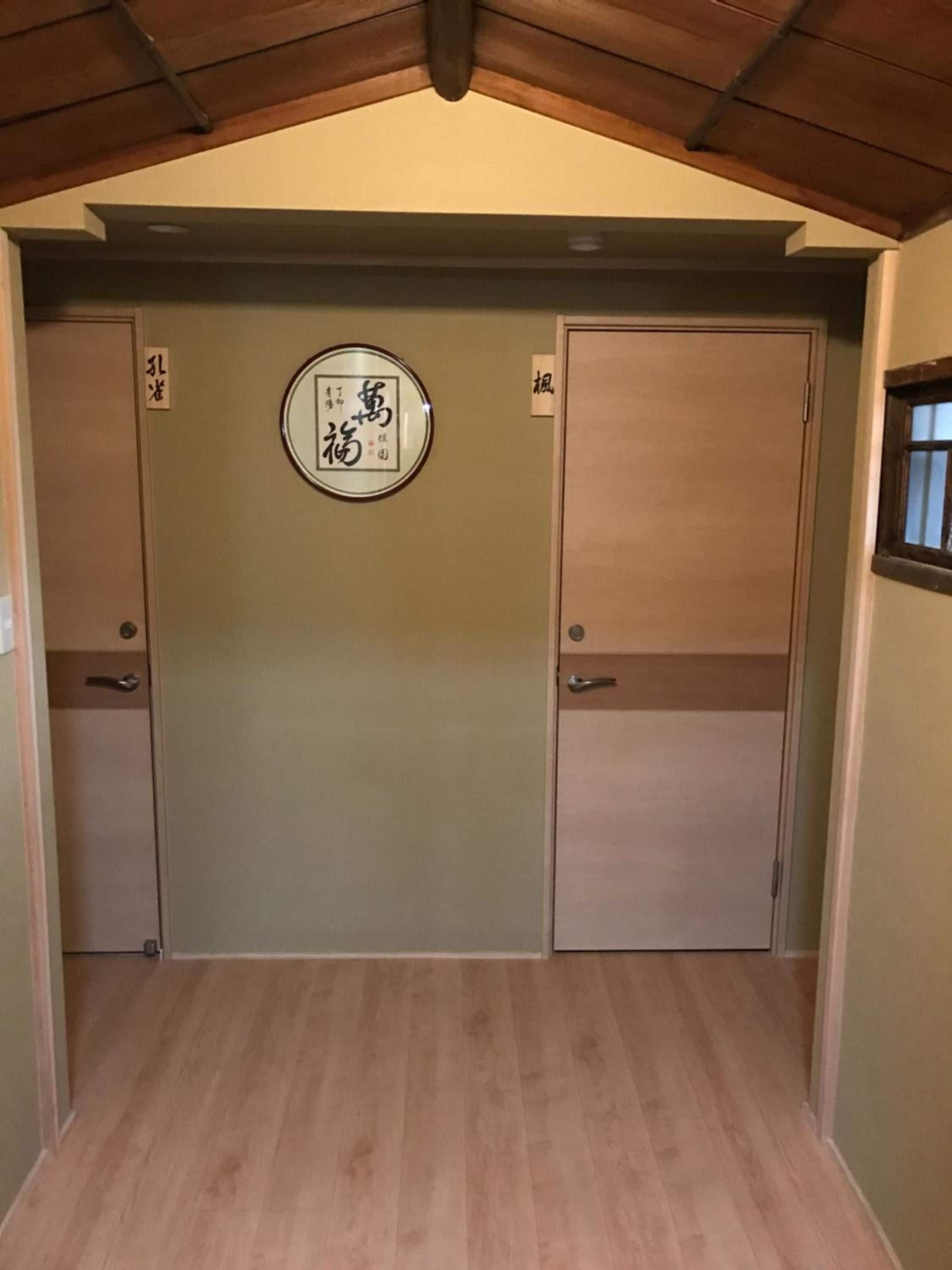 Une pièce avec un plafond en bois, une grande porte ornée d’une enseigne circulaire et une fenêtre sur le côté droit.