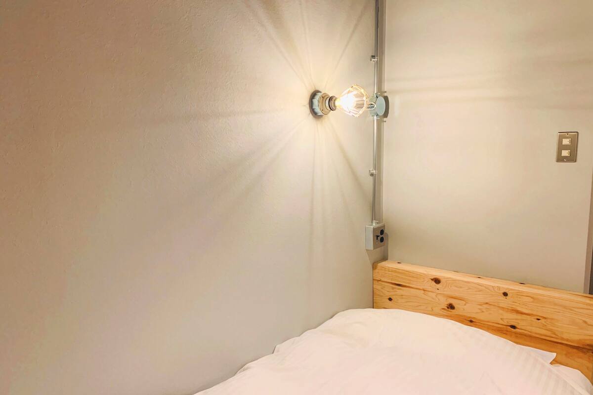 A single bed with a wooden headboard in a room with a light fixture on the wall.