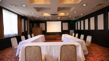 Un salón de conferencias con una larga mesa, sillas, una pantalla de proyector y piso alfombrado.