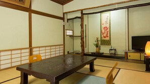 Une pièce de style japonais traditionnel, avec un sol recouvert de tatamis, une table basse, un canapé et un téléviseur.