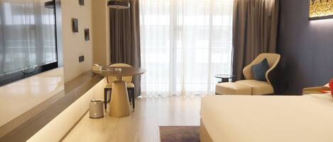 A hotel room with a bed, a desk, a chair, a TV, and a large window with curtains.