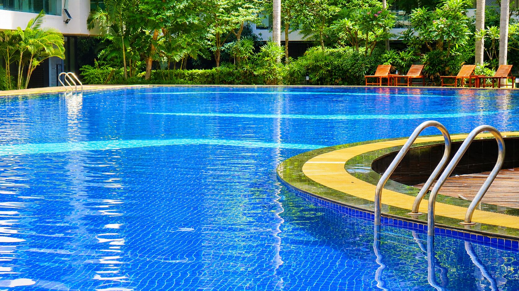 A clear blue swimming pool with a wooden deck and metal handrails.