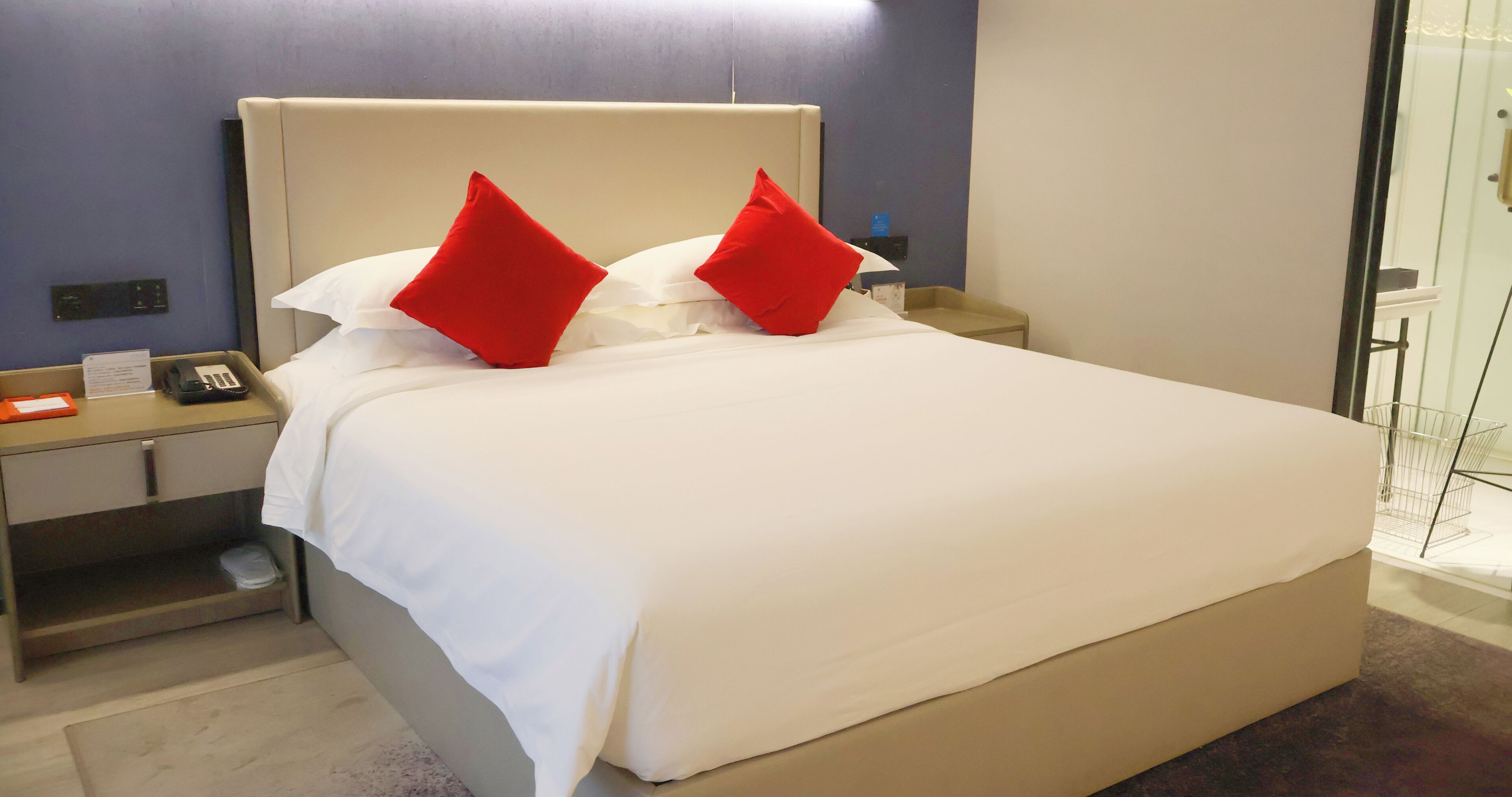 A hotel room with a bed, a nightstand, a telephone, and a glass partition.