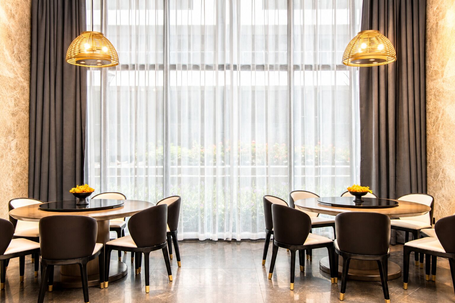 A dining area with round tables, chairs, and two hanging lamps.