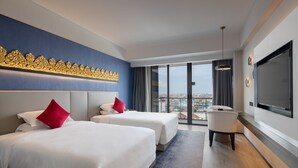 Een hotelkamer met twee bedden, een grote televisie en uitzicht op de stad.