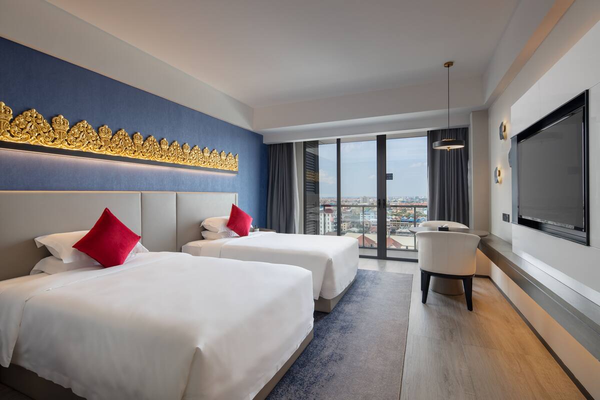 Ein Hotelzimmer mit zwei Betten, einem großen Fernseher und Blick auf die Stadt.