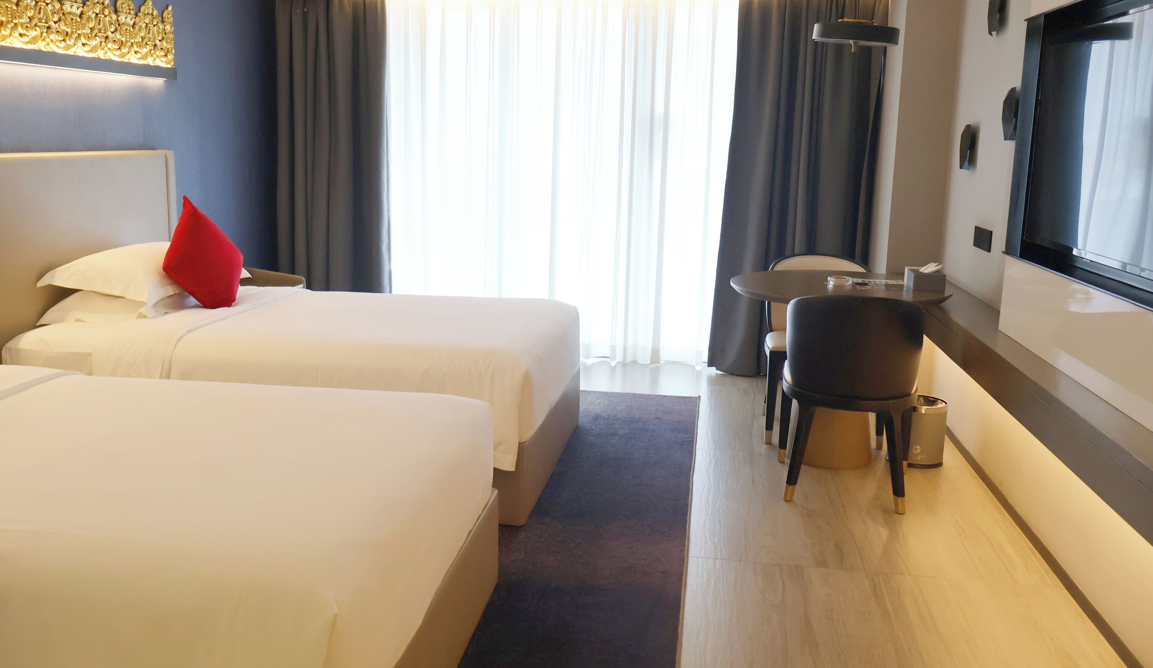 Hotelkamer met twee bedden, een tafeltje, een stoel, een televisie en een raam met gordijnen.