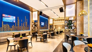 Een modern restaurant met een blauwe accentmuur, verschillende zithoeken en een open keuken.
