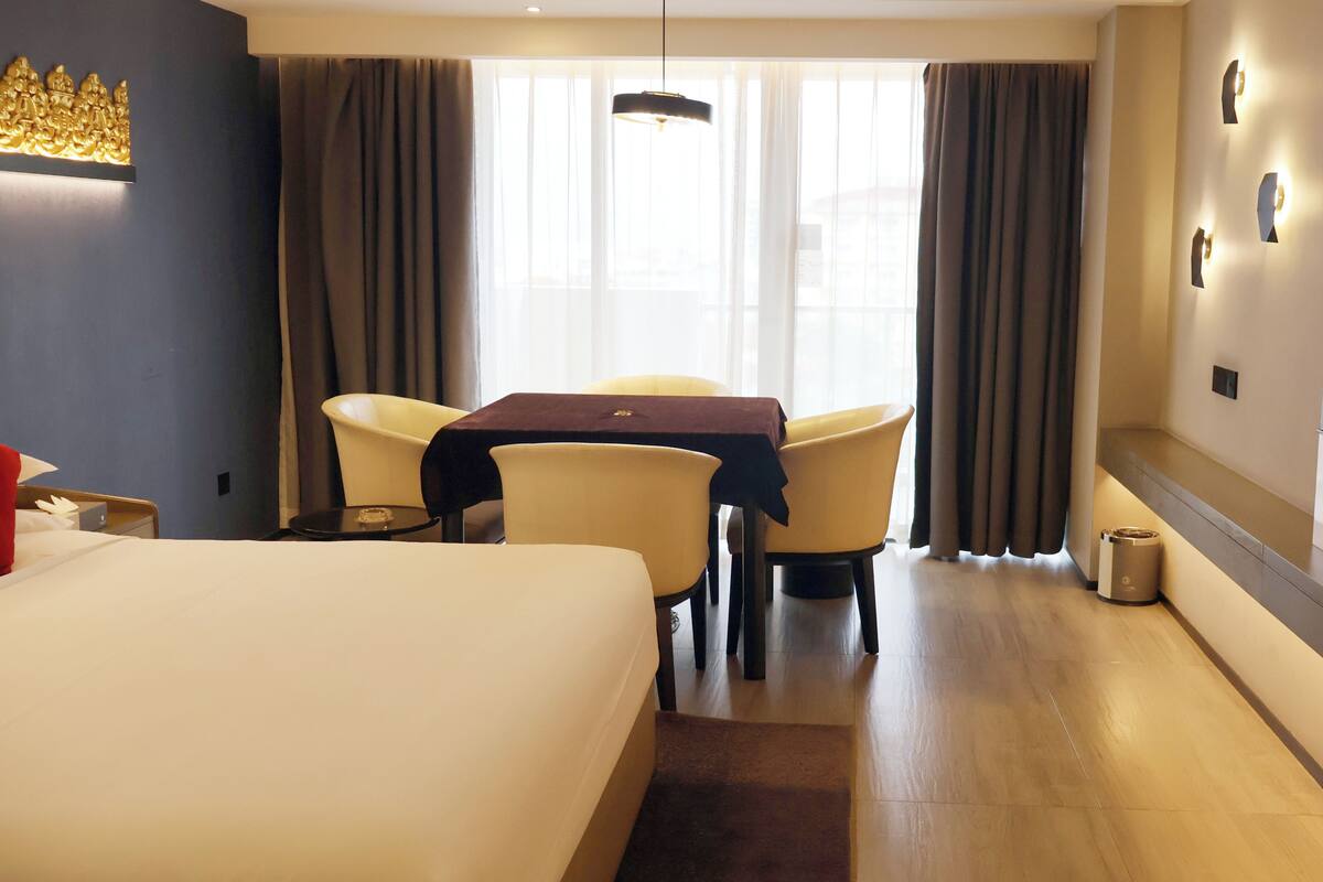 Ein Hotelzimmer mit einem Bett, einem Tisch mit Stühlen, einem Fernseher und einem Fenster mit Vorhängen.