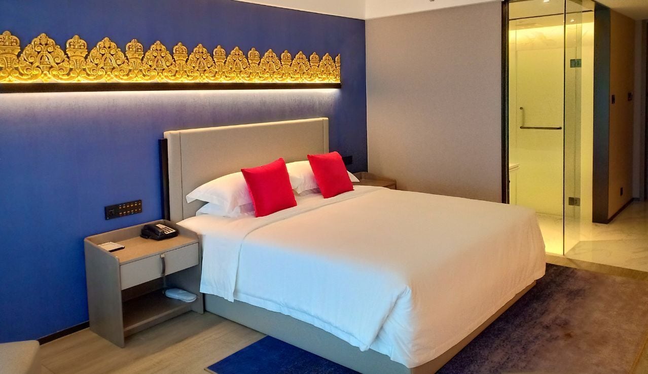 A hotel room with a large bed, a nightstand, a phone, and a decorative wall panel.
