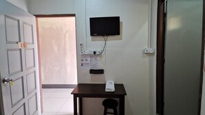 A small room with a door labeled '15', a table with a folded towel, a chair, a wall-mounted TV, and a power outlet with a plug. - Lodge88 2 (Ranau)
