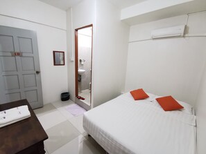 A bedroom with a bed, a nightstand, a dresser, a bathroom with a sink and mirror, and an air conditioning unit.