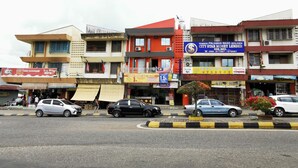 A street view with multiple commercial buildings, including a prominent red building with a blue sign advertising a money lender service. - Lodge88 2 (Ranau)