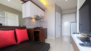 Ein modernes Wohnzimmer mit einem dunkelgrauen Sofa, roten Kissen, einer Küchenzeile mit Herd und einem Fernseher.