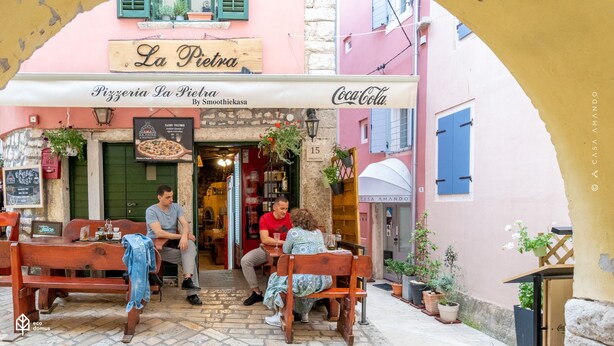 An outdoor café with wooden benches and tables, a pizzeria sign, and a Coca-Cola sign. - Casa Amando Eco Boutique House (Rovinj)