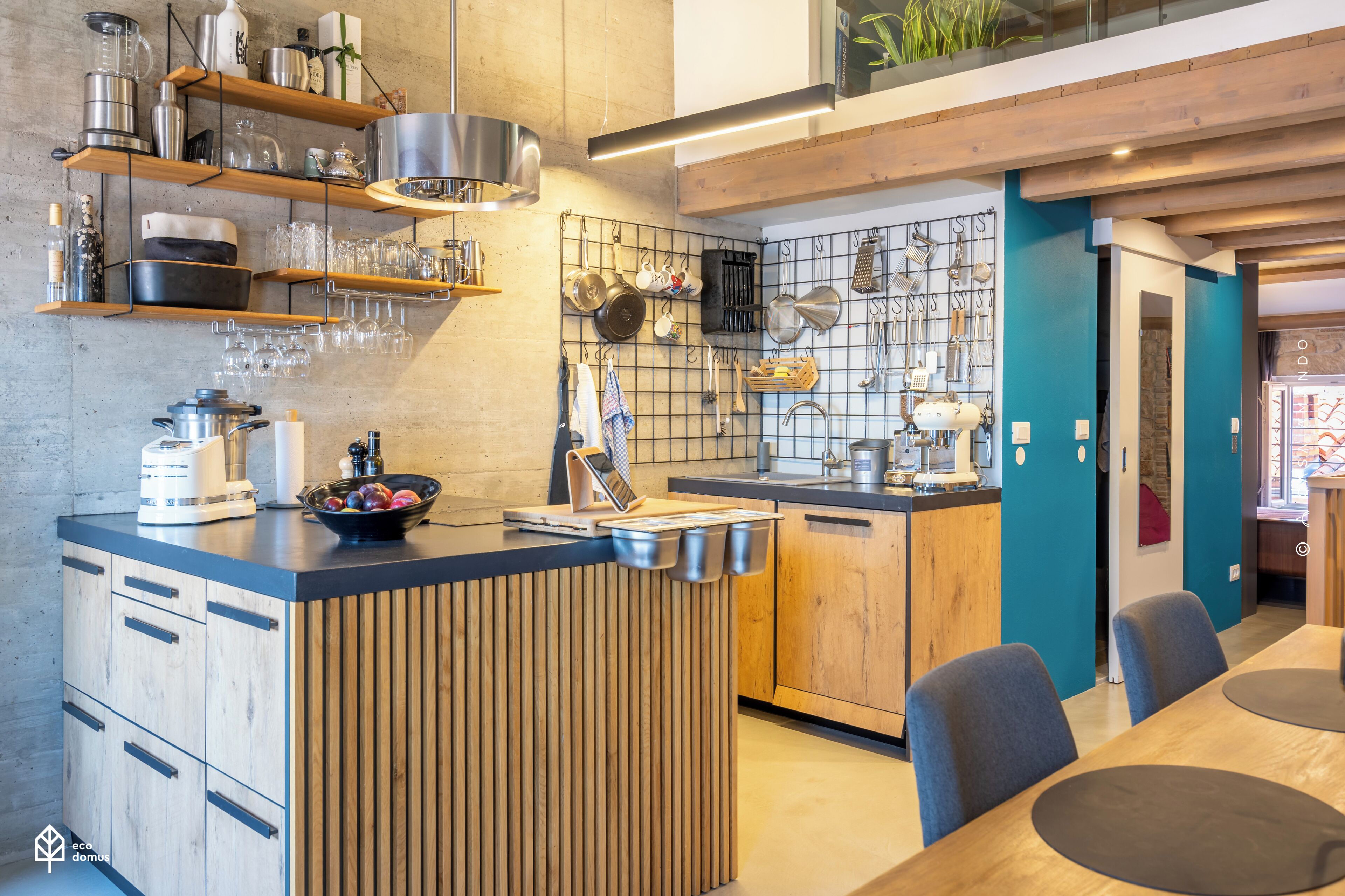 Een moderne keuken met houten keukenkastjes, een centraal kookeiland en diverse keukengerei en benodigdheden die op planken en haken staan uitgestald.
