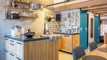 Een moderne keuken met houten keukenkastjes, een centraal kookeiland en diverse keukengerei en benodigdheden die op planken en haken staan uitgestald.