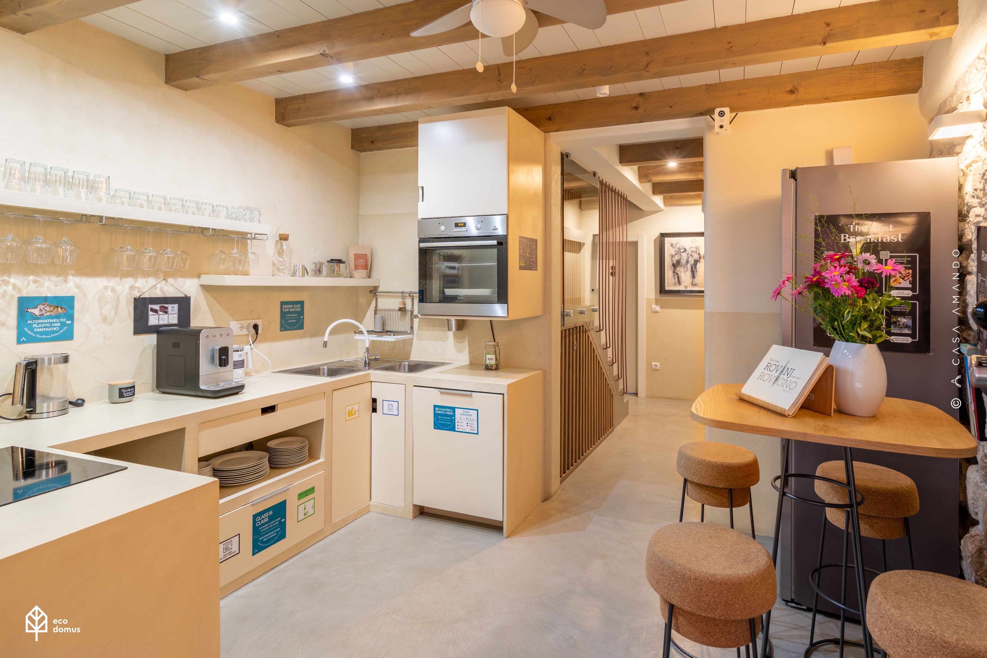 A modern kitchen with a built-in oven, a coffee machine, and a small dining area with stools.