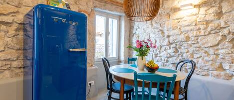 A dining area with a stone wall, a blue refrigerator, a wooden table, and teal chairs.