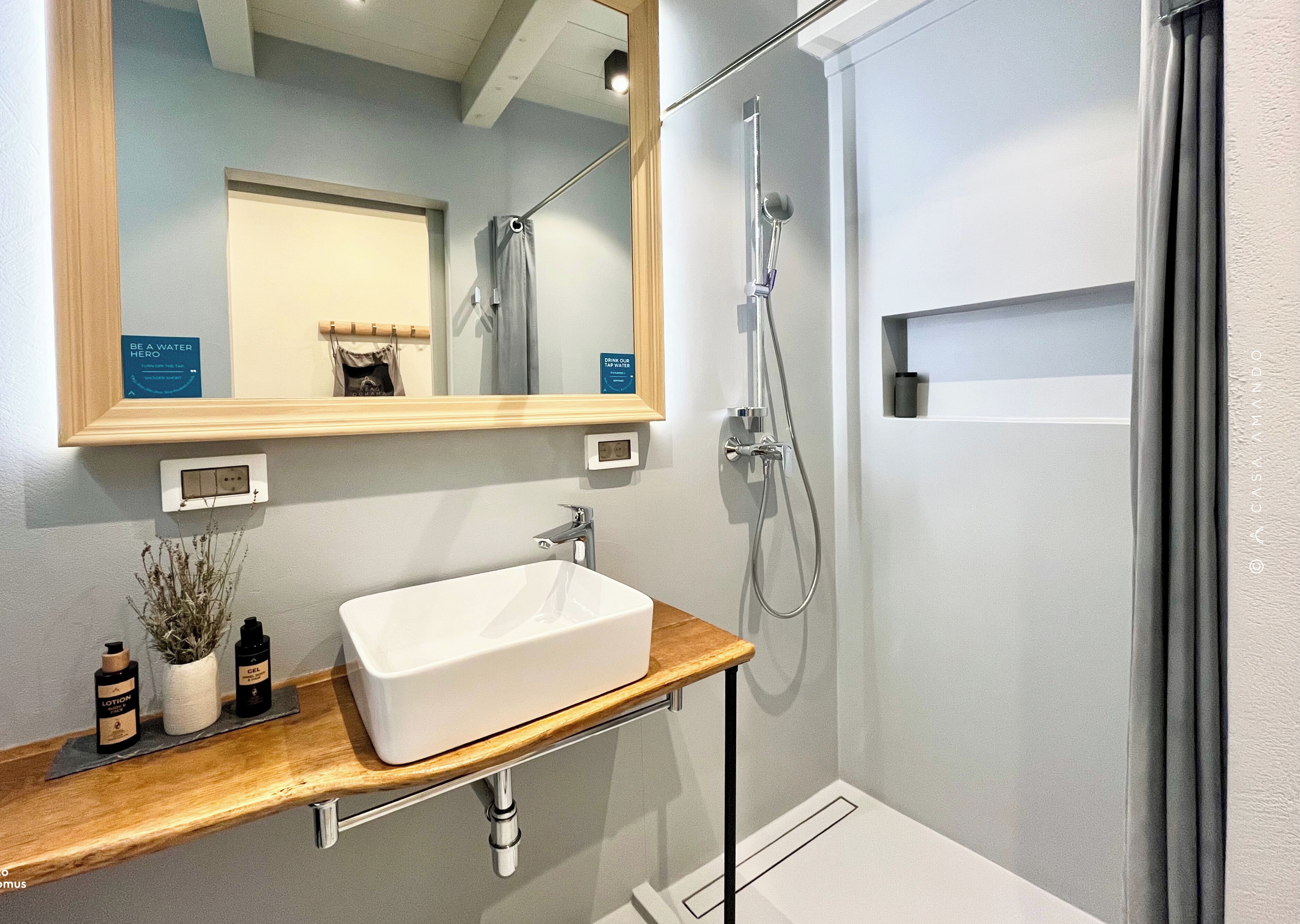 A bathroom with a white sink, a mirror, a shower, and a wooden vanity.