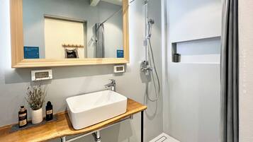 A bathroom with a white sink, a mirror, a shower, and a wooden vanity.