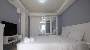A modern hotel room with a large bed, a TV on a stand, and a bathroom visible through an open door. - Best Deal Studio Bassura Apartment (Jakarta)