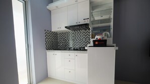 A modern kitchen with white cabinets, a black and white tiled backsplash, and a travelio coffee machine on the counter. - Best Deal Studio Bassura Apartment (Jakarta)