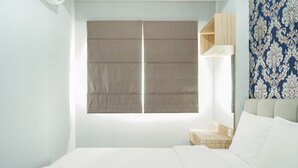 A hotel room with a bed, a window with a blind, a bedside table, and a patterned wall.