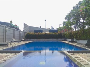 A swimming pool with lounge chairs, a hedge, and a building with satellite dishes.