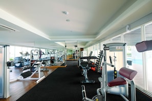 A gym with various exercise machines, a mirrored wall, and large windows.
