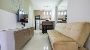 A modern kitchen with a flat-screen TV, stainless steel appliances, and a beige sofa in a bright, well-lit room.