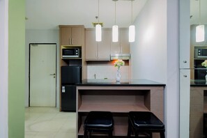 A compact kitchen with a microwave, stove, and a small dining area with stools. - 2BR with Sofa Bed Cervino Tebet Apartment (Jakarta)