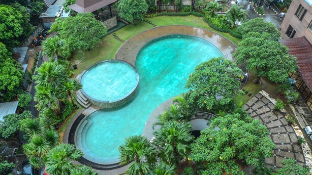 A rooftop swimming pool with two separate sections, surrounded by lush greenery and a stone pathway.
