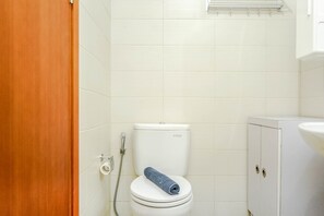 A bathroom with a white toilet, a towel on the seat, and a shower head. - New Furnished Studio Apartment @ Woodland Park Residence (Jakarta)