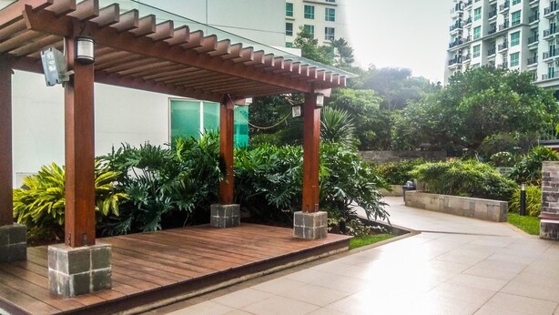 A covered outdoor area with wooden pillars, surrounded by greenery and a tiled floor. - New Furnished Studio Apartment @ Woodland Park Residence (Jakarta)