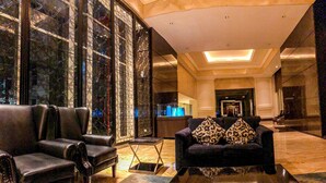 A lobby with leather sofas, a glass partition, and a reception desk. - Homey 2BR Apartment @ Casa Grande Residence (Jakarta)