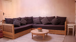 Een moderne woonkamer met een hoekbank, een ronde houten salontafel en een klein witte bijzettafeltje.