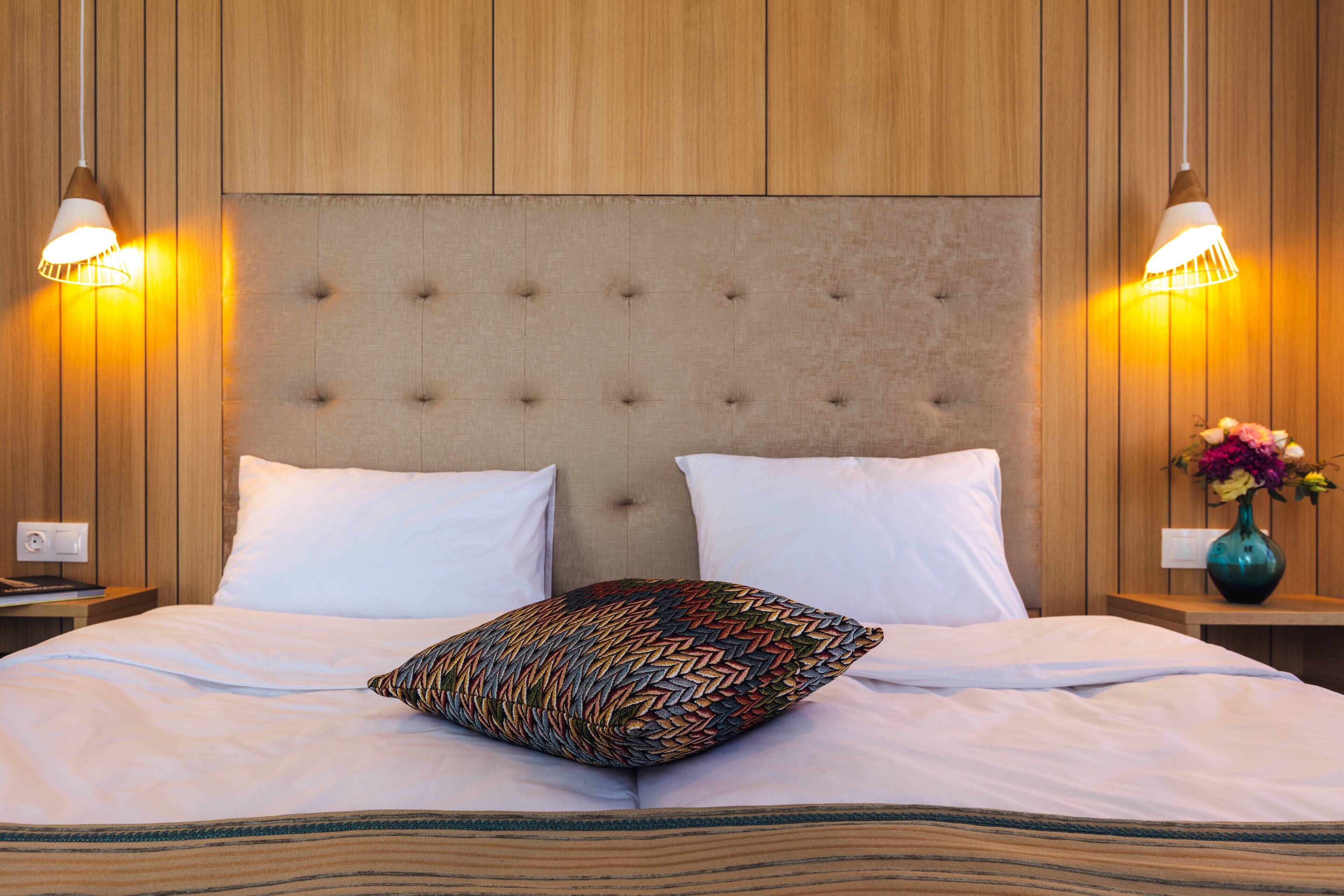 A neatly made bed with a tufted headboard, two bedside lamps, and a vase with flowers on the nightstand.