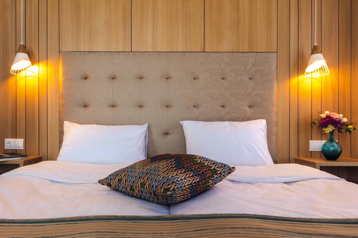 A neatly made bed with a tufted headboard, two bedside lamps, and a vase with flowers on the nightstand.