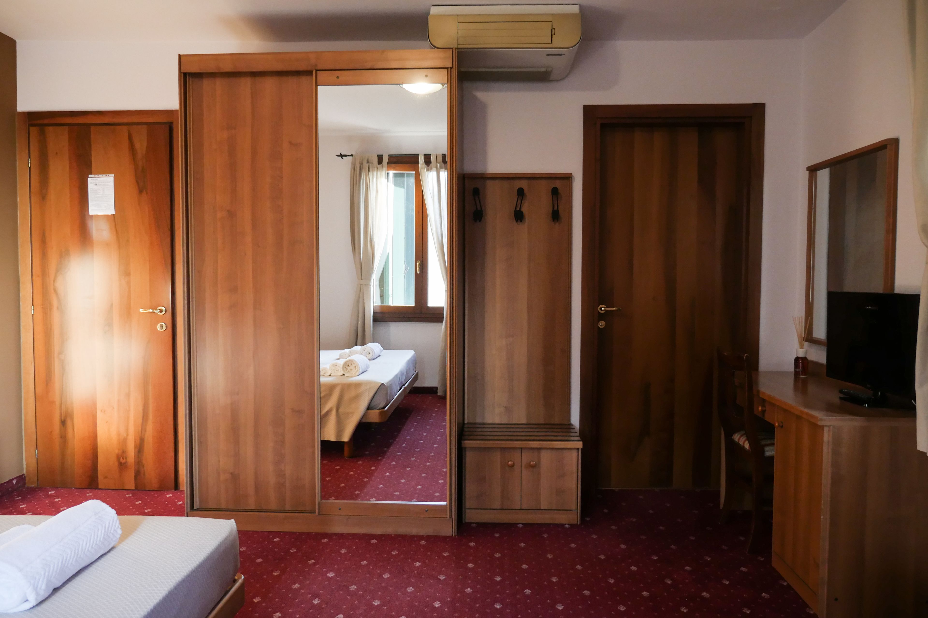 A hotel room with a bed, a wardrobe, a mirror, a television, and a small cabinet.