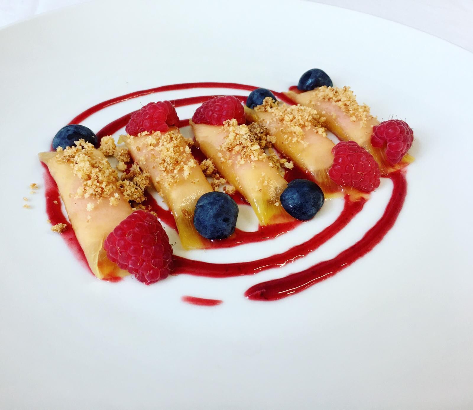 A dessert plate with fruit-topped pastries and a red sauce swirl.