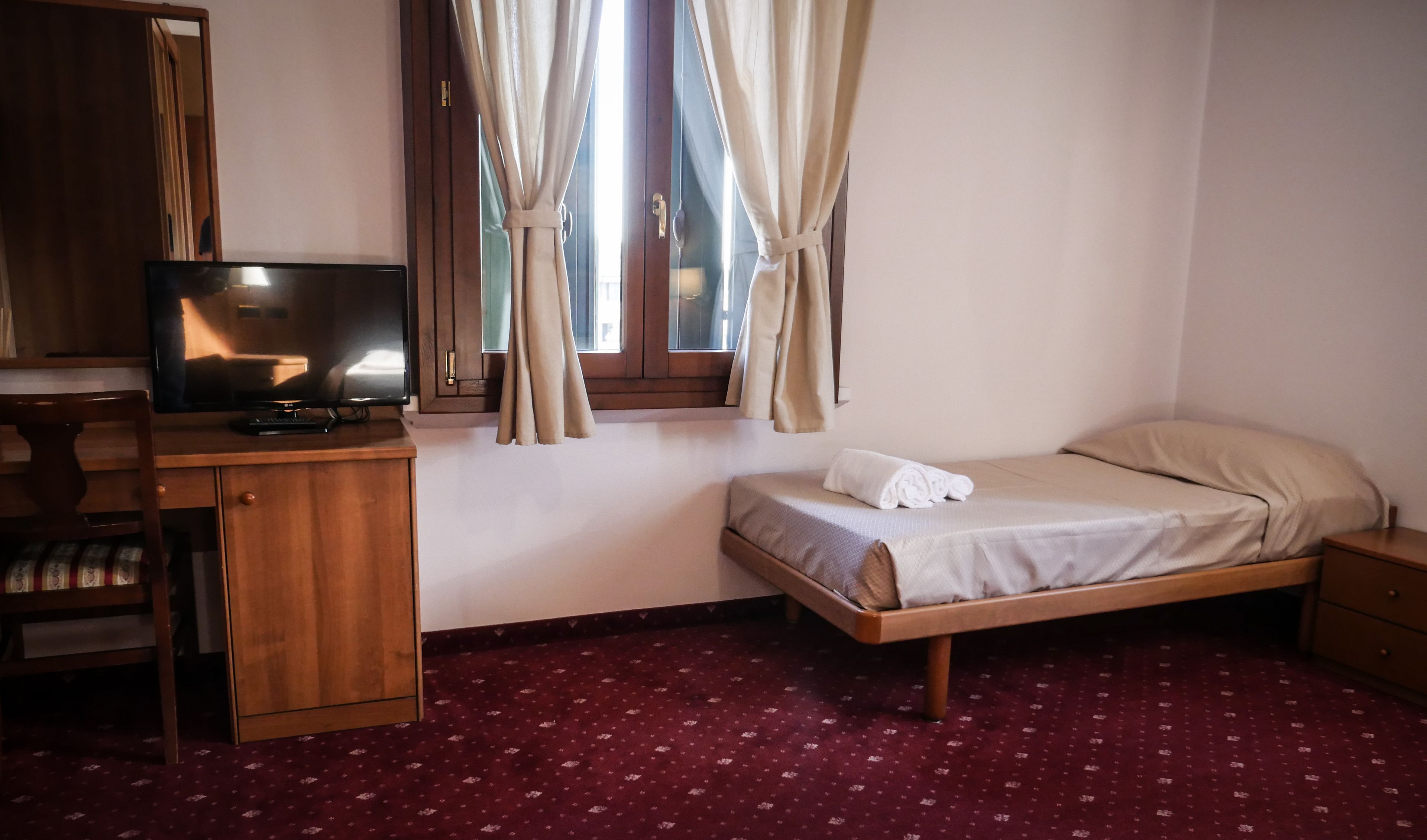 Ein Hotelzimmer mit einem Bett, einem Fernseher auf einer Holzkommode und einem Fenster mit Vorhängen.