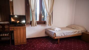 Ein Hotelzimmer mit einem Bett, einem Fernseher auf einer Holzkommode und einem Fenster mit Vorhängen.