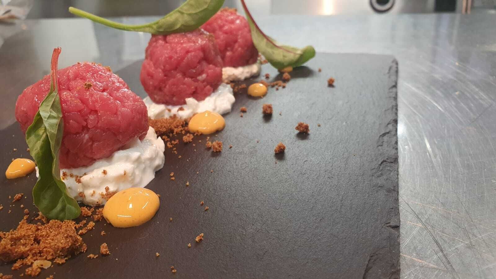 A dessert with raspberries, cream, and crumbled chocolate on a slate plate.