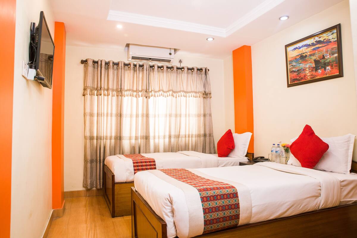 Quarto de hotel com duas camas, televisão, ar condicionado e um quadro na parede.