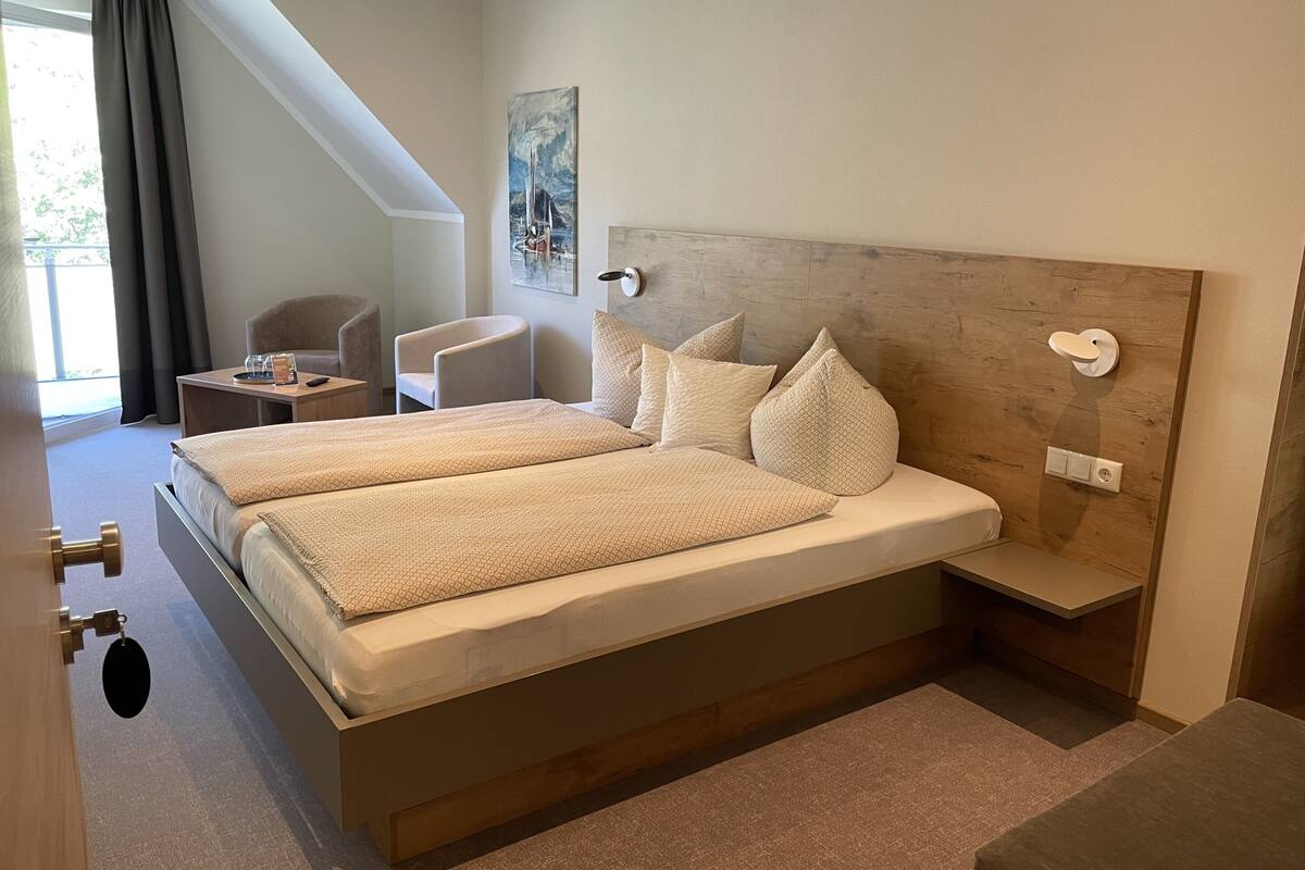 A double bed with a wooden headboard, two bedside tables, a chair, and a painting on the wall.